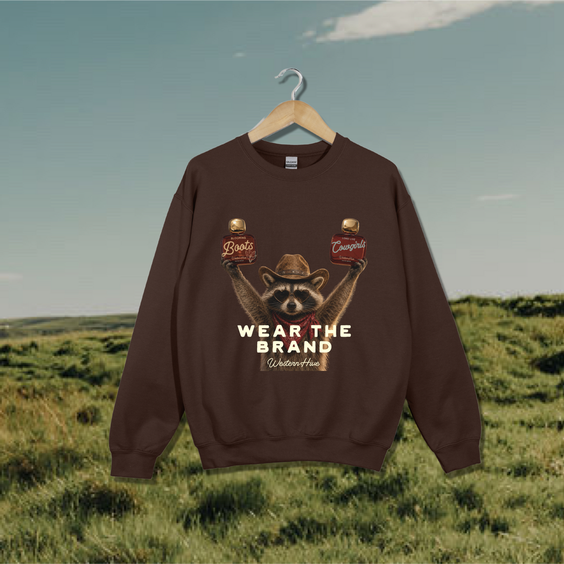 The sweatshirt features a graphic of a raccoon wearing a cowboy hat and holding two Western Hive perfumes &