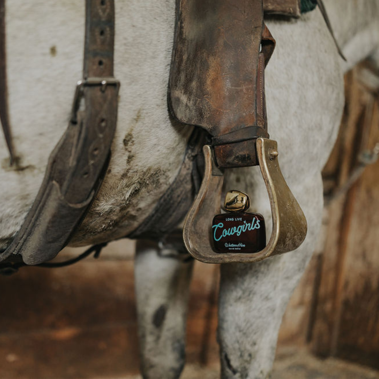Long Live Cowgirls perfume displayed in a saddle stirrup on horseback, inspired by western ranch life.